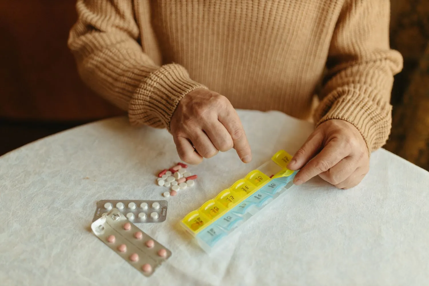 Hands sorting daily pills into a weekly medication organizer